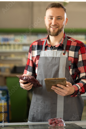 Fotografia portrait of a smiling sales clerk wearing apron using a digital tablet working i
