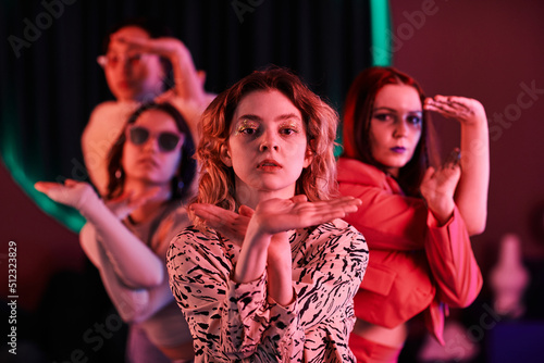 Waist up portrait of vogue dance crew posing in pink neon light, focus on girl with glitter makeup