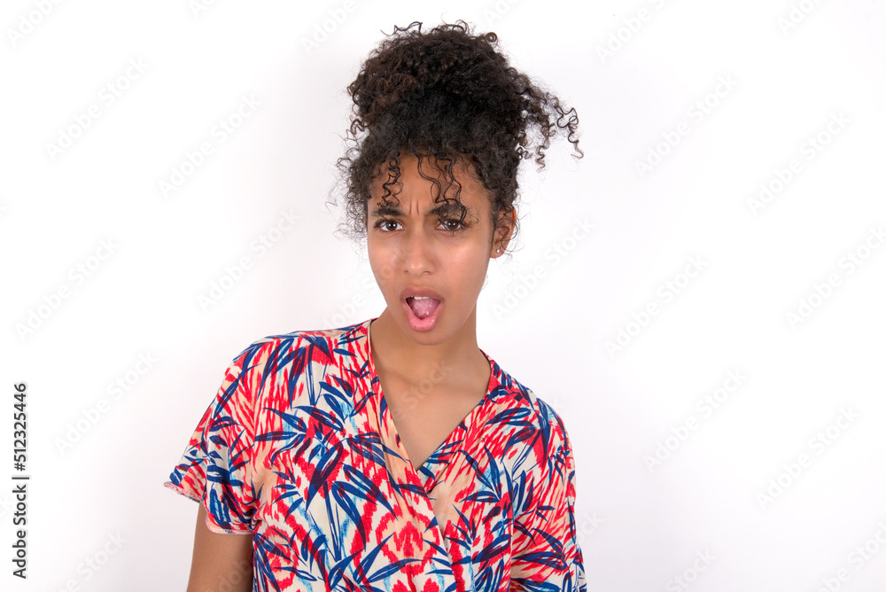 Expressive facial expressions. Shocked stupefied Young African American woman wearing colourful dress over white wall, keeps jaw dropped feels stunned from what he sees aside. Expressive facial expressions. Shocked stupefied Young African American woman wearing colourful dress over white wall, keeps jaw dropped feels stunned from what he sees aside.