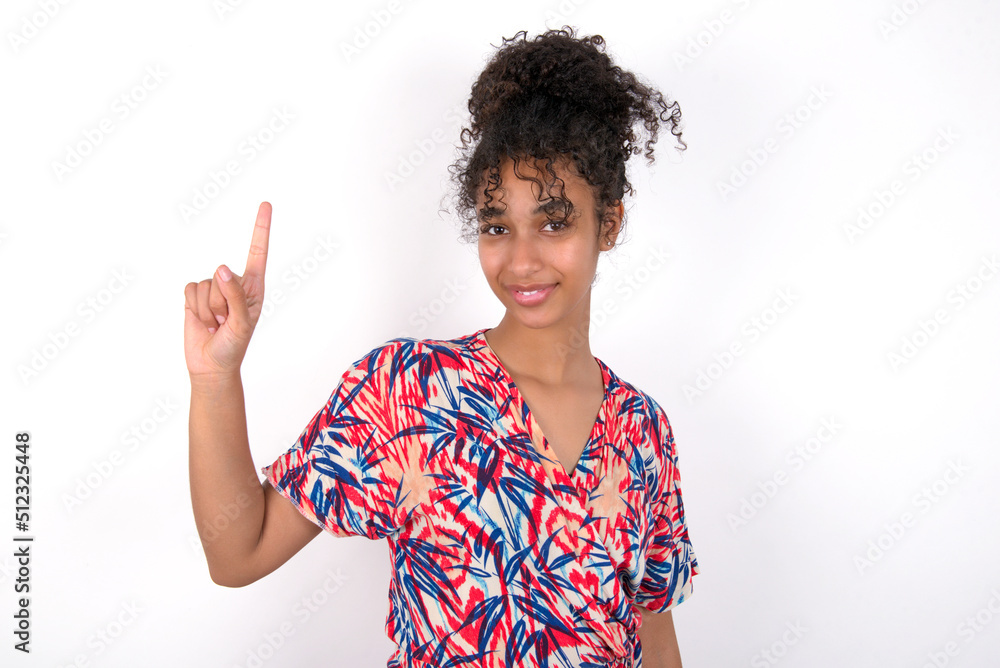 Young African American woman wearing colourful dress over white wall showing and pointing up with fingers number one while smiling confident and happy. Young African American woman wearing colourful dress over white wall showing and pointing up with fingers number one while smiling confident and happy.