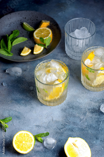 citrus lemonade with mint and lemon in the glass with ice cubes. fresh ingredients lemon and mint on gray ceramic plate