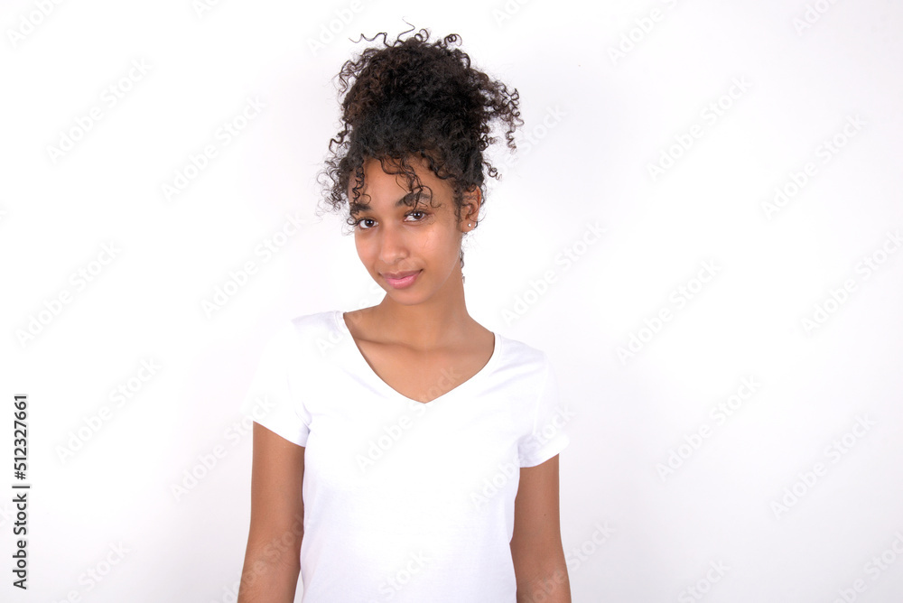 Young beautiful girl with afro hairstyle wearing white t-shirt over white wall with nice beaming smile pleased expression. Positive emotions concept Young beautiful girl with afro hairstyle wearing white t-shirt over white wall with nice beaming smile pleased expression. Positive emotions concept