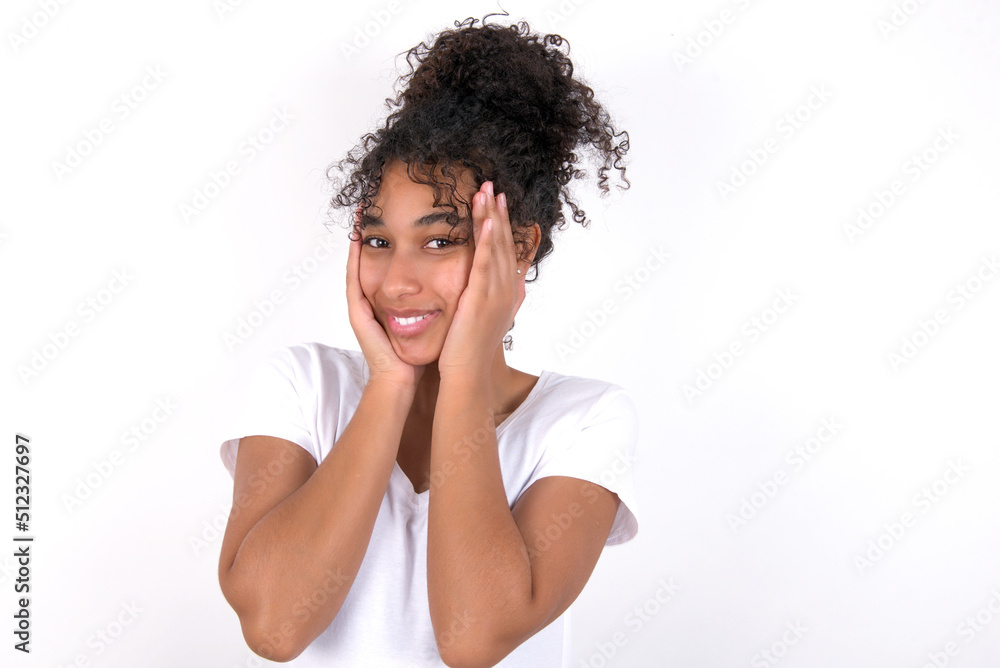 Young beautiful girl with afro hairstyle wearing white t-shirt over white wall Pleasant looking cheerful, Happy reaction Young beautiful girl with afro hairstyle wearing white t-shirt over white wall Pleasant looking cheerful, Happy reaction