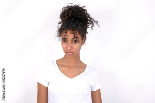 Offended dissatisfied Young beautiful girl with afro hairstyle wearing white t-shirt over white wall with moody displeased expression at camera being disappointed by something