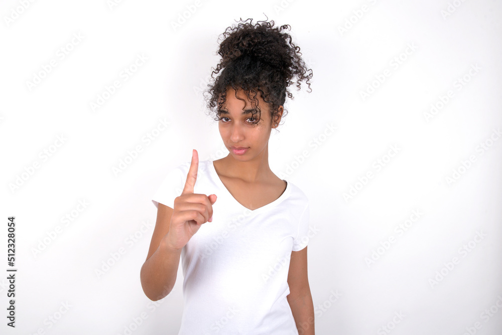 Young beautiful girl with afro hairstyle wearing white t-shirt over white wall frustrated and pointing to the front Young beautiful girl with afro hairstyle wearing white t-shirt over white wall frustrated and pointing to the front