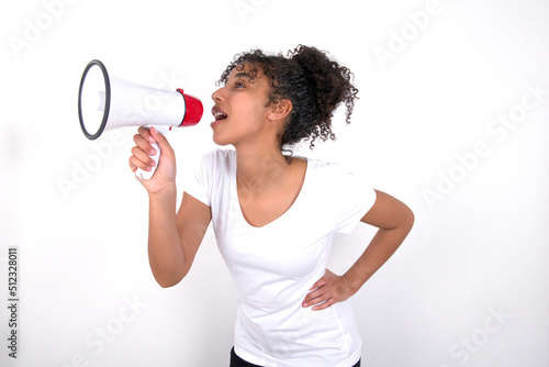 Funny Young beautiful girl with afro hairstyle wearing white t-shirt over white wall People sincere emotions lifestyle concept. Mock up copy space. Screaming in megaphone.