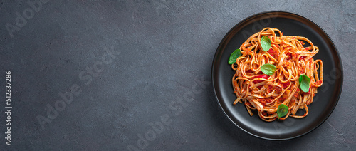 Pasta with tomato sauce and fresh basil on a dark background. View from above. Vegetarian food.