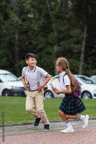 Multiethnic classmates with notebooks running outdoors.