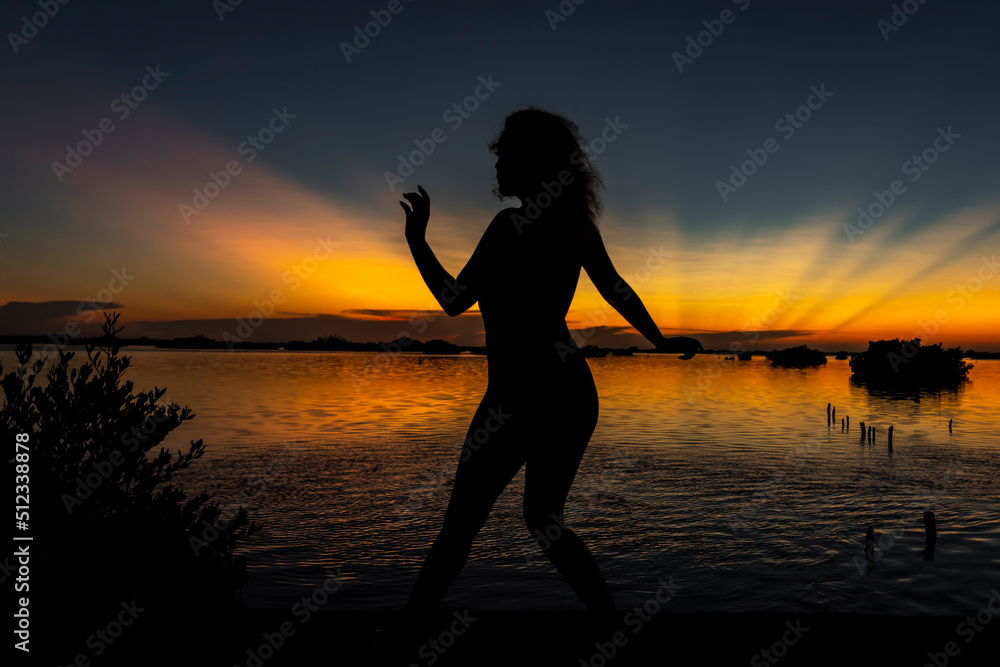 A Lovely Nude Latin Model Is Silhouetted As She Poses With The Rising Sun Behind Her On A Romantic Caribbean Beach