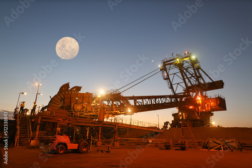 Early morning sunrise of beautiful isolated massive iron ore reclaimer industry mining heavy duty equipment machinery with full moon at the background