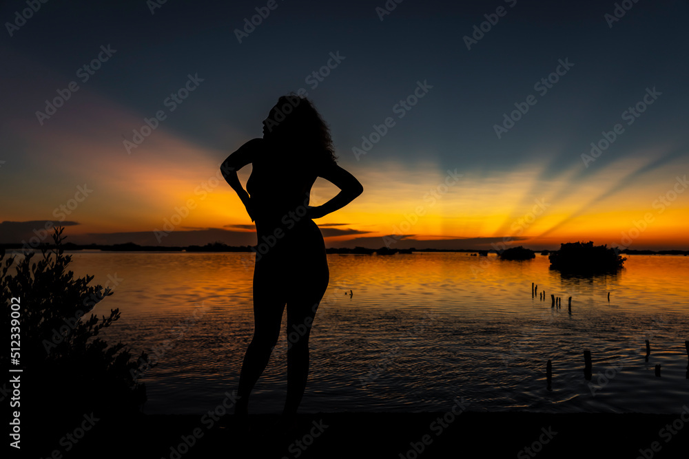 A Lovely Nude Latin Model Is Silhouetted As She Poses With The Rising Sun Behind Her On A Romantic Caribbean Beach