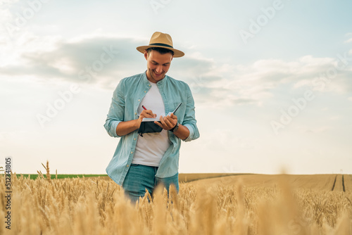 Happy farmer  writing notes  while standing in his growing  wheat  field.
