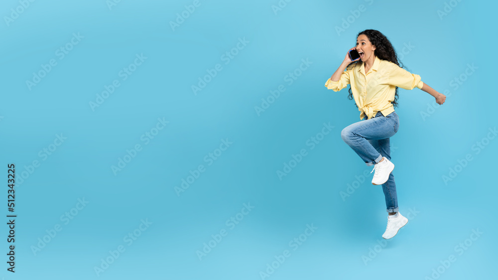 Excited young woman talking on mobile phone, making call, jumping and running on yellow background, blank space Excited young woman talking on mobile phone, making call, jumping and running on yellow background, blank space