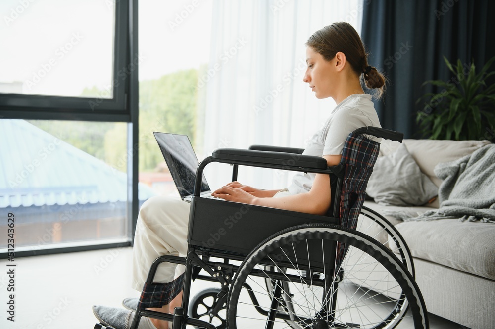 Female freelance programmer sitting in wheelchair and using computers while coding web game at home. Female freelance programmer sitting in wheelchair and using computers while coding web game at home.