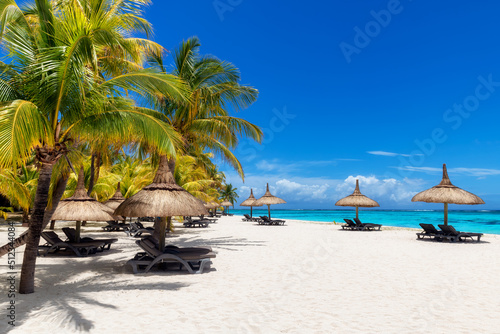 Fototapeta Naklejka Na Ścianę i Meble -  Beautiful vacations beach with palm trees and straw umbrellas in tropical resort in Paradise island.