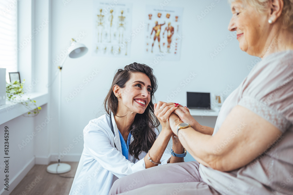 Health visitor and a senior woman during doctors visit. Patient is holding caregiver for a hand while spending time together. Caring young nurse support assist positive old lady patient Health visitor and a senior woman during doctors visit. Patient is holding caregiver for a hand while spending time together. Caring young nurse support assist positive old lady patient