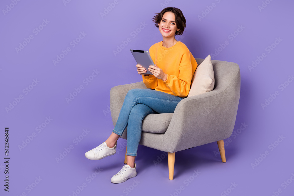 Portrait of attractive cheerful girl sitting using gadget reading e book isolated over violet lilac color background Portrait of attractive cheerful girl sitting using gadget reading e book isolated over violet lilac color background