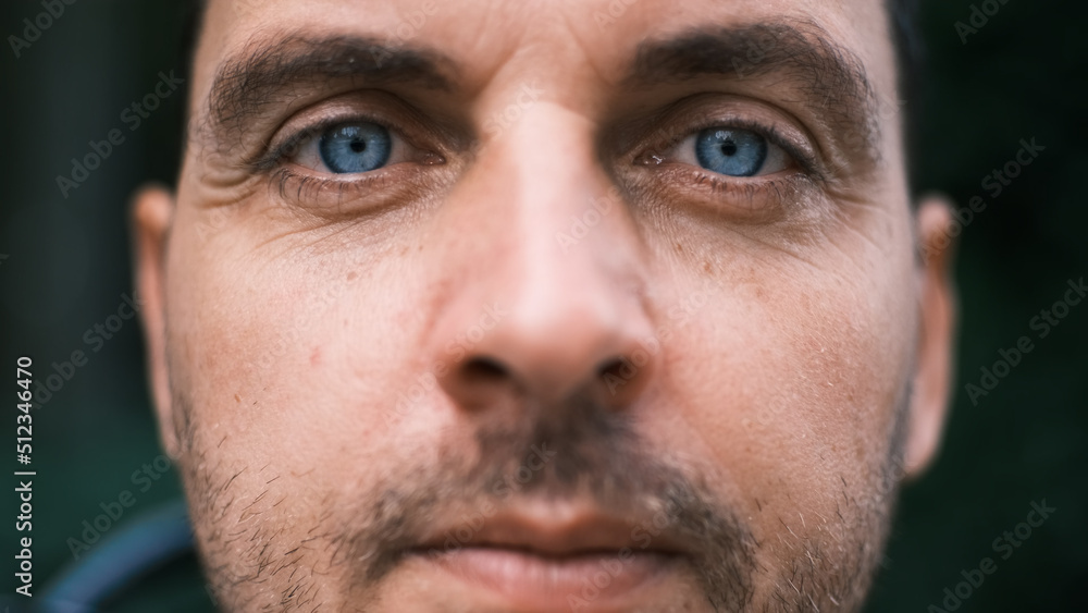 Fototapeta premium Close-up face of a young man with bright blue eyes looking seriously with curiosity