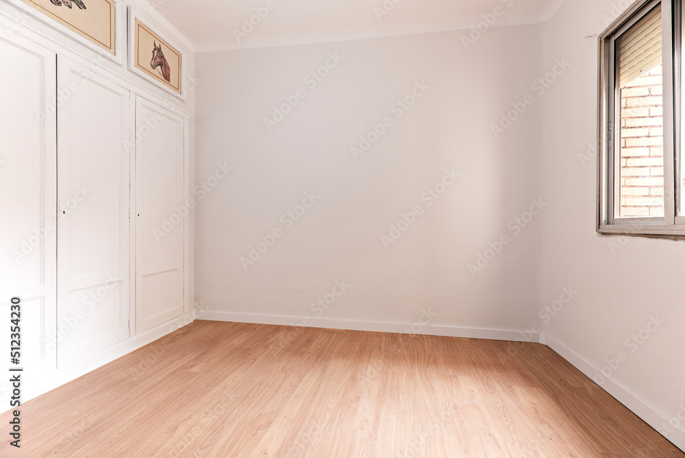 Empty room with oak parquet floor, white painted walls, built-in wardrobe with wooden doors and aluminum window Empty room with oak parquet floor, white painted walls, built-in wardrobe with wooden doors and aluminum window