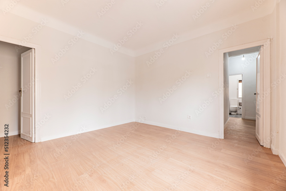 Empty room with oak parquet floor, plain white painted walls and white woodwork and bathroom in another room Empty room with oak parquet floor, plain white painted walls and white woodwork and bathroom in another room