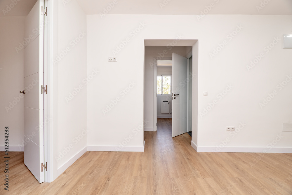 Obraz premium Empty living room with plain white painted walls, several access doors to other rooms with aluminum windows, white carpentry, doors and lamps and light oak floor