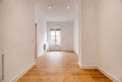 Empty room with oak parquet flooring and woodwork on doors and balcony, basket-handle arch separating rooms and light oak flooring