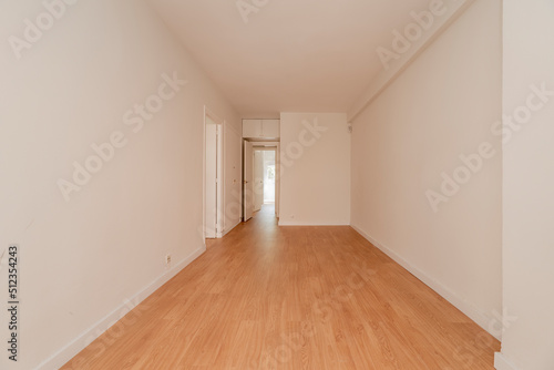 Empty room with access doors to other rooms, wooden floors and plain white painted walls © Toyakisfoto.photos