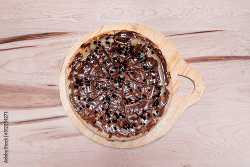 Sweet pizza with Spanish nocilla, pieces of chocolate cookie on wooden table