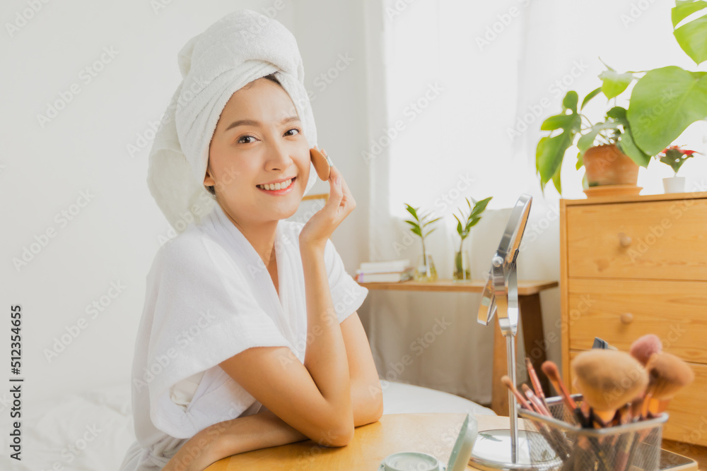 Beautiful Asian woman applying foundation to make up her face at home Beautiful Asian woman applying foundation to make up her face at home