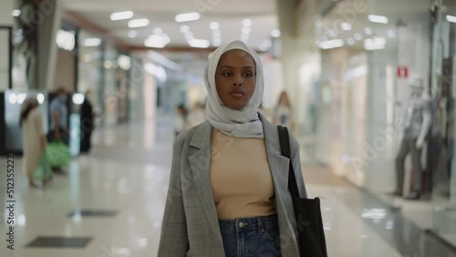 Confident African-American woman with chiffon hijab walks along hallway gallery in trade mall slow motion. Muslim lady visits shopping center photo