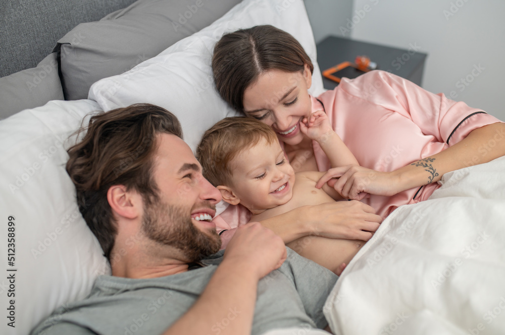 Woman and man touching baby lying on bed Woman and man touching baby lying on bed