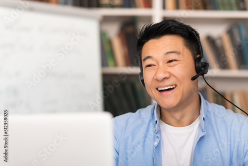 Asian Man Video Calling Via Laptop Wearing Headset In Library