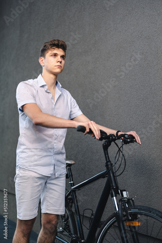 Young modern looking blond man posing with a bike against gray wall background
