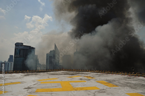 Manila, Philippines - July 11, 2013: large gray smoke reaches the top of a tall building with a helipad. The two-hour fire burned down hundreds of shanties in the financial district of Makati City. photo