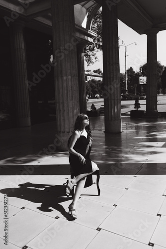 A beautiful girl with a hairstyle in a black dress on the street with a cigarette in her hands smokes, black and white photo.
