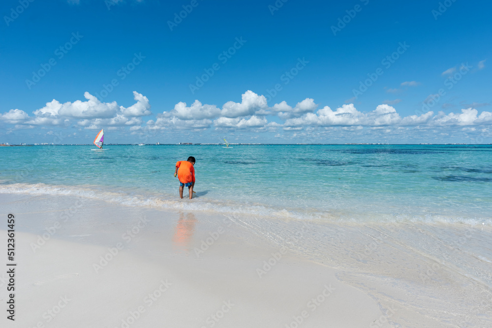 A child plays by the sea at a tropical beach in Isla Mujeres Mexico, during school vacations