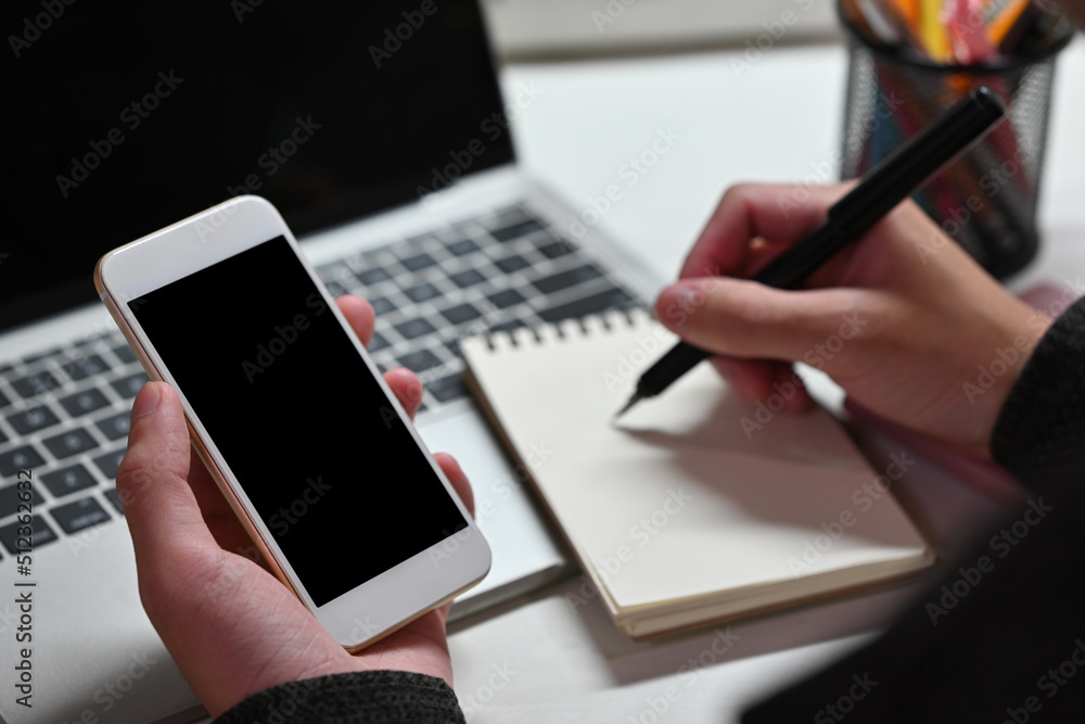 Close up of a man sitting in the office working on a laptop, using a smart phone and taking a note. For business, technology and home concept. Close up of a man sitting in the office working on a laptop, using a smart phone and taking a note. For business, technology and home concept.