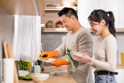 Loving asian couple washing dishes together at home