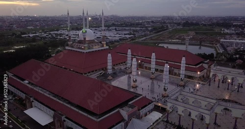 Moving drone shot of the great Mosque of Central Java (MAJT) in suset time. Th sun is orange and the weather is cloudy. It have some pillars and some umbrela that is closed photo