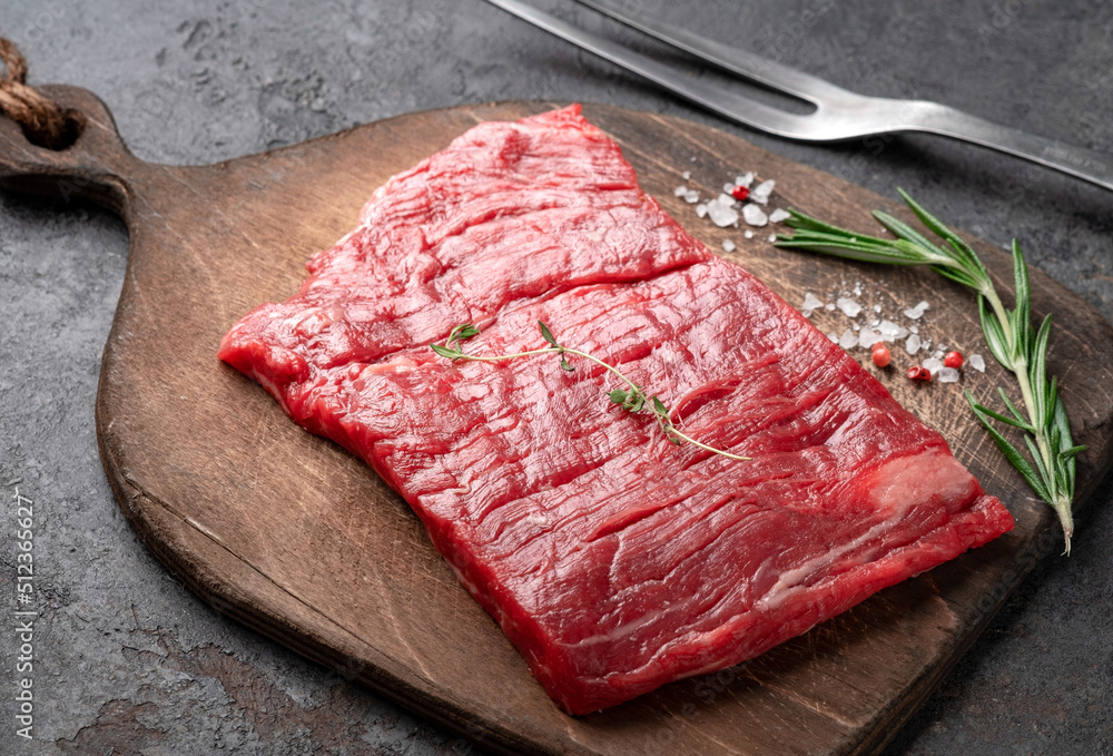 Raw flank steak or Outside skirt steak on a wooden board with grilling seasonings, close up - obrazy, fototapety, plakaty 