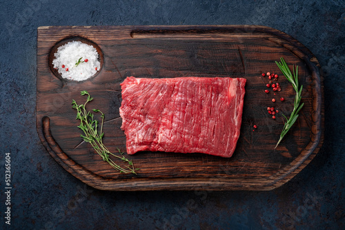 Raw flank steak on a wooden board with grilling seasonings