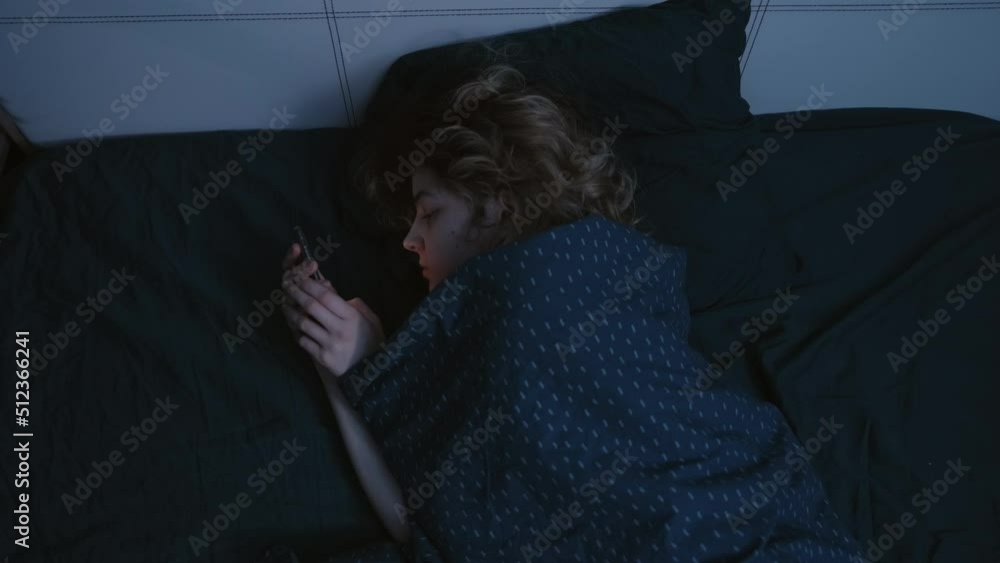 A young woman lies on her side in bed with a phone in her hands at night, looks into it and falls asleep. Slow motion 4k footage A young woman lies on her side in bed with a phone in her hands at night, looks into it and falls asleep. Slow motion 4k footage