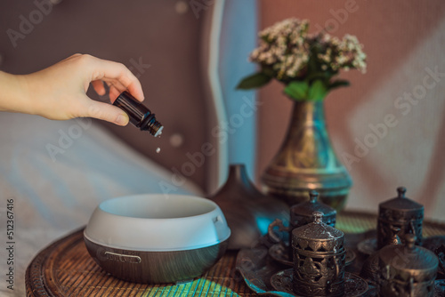 Woman adding essential oil to aroma diffuser on table photo
