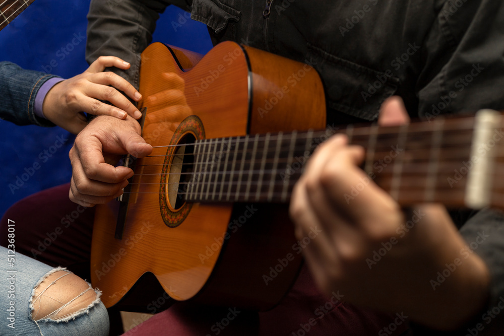 Fototapeta premium Unrecognizable Latin American teacher corrects right hand posture on guitar strings. Concept music lessons