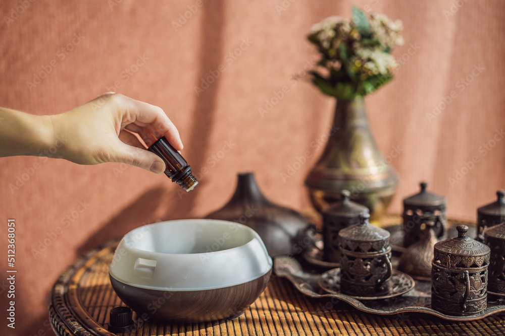 Obraz premium Woman adding essential oil to aroma diffuser on table