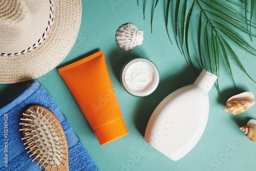 Summer travel beach essentials flat lay photography. Straw hat, towel, shampoo, sunscreen tube, wooden comb, palm leaves and seashells. Natural cosmetic products for hair and skin care