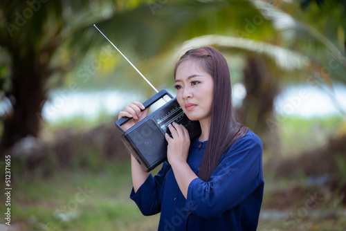 Portrait beautiful happiness asian farmer wearing blue Mauhom shirt and hat under listen music for vintage radio relaxed between work with green nature background. photo