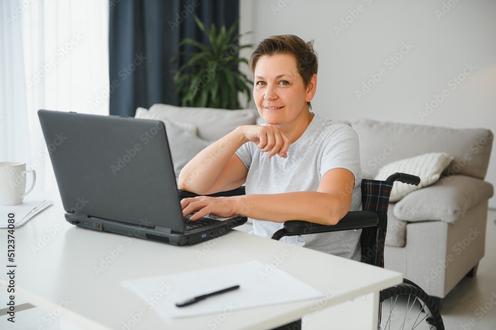 Positive elderly woman in wheelchair working on laptop, IT freelancer, online Positive elderly woman in wheelchair working on laptop, IT freelancer, online