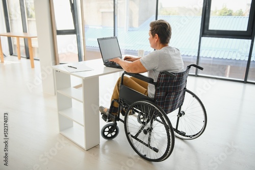 Middle age woman using laptop sitting on wheelchair at home