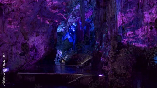 Tourists entering chamber of St. Michael's cave lit by purple light.